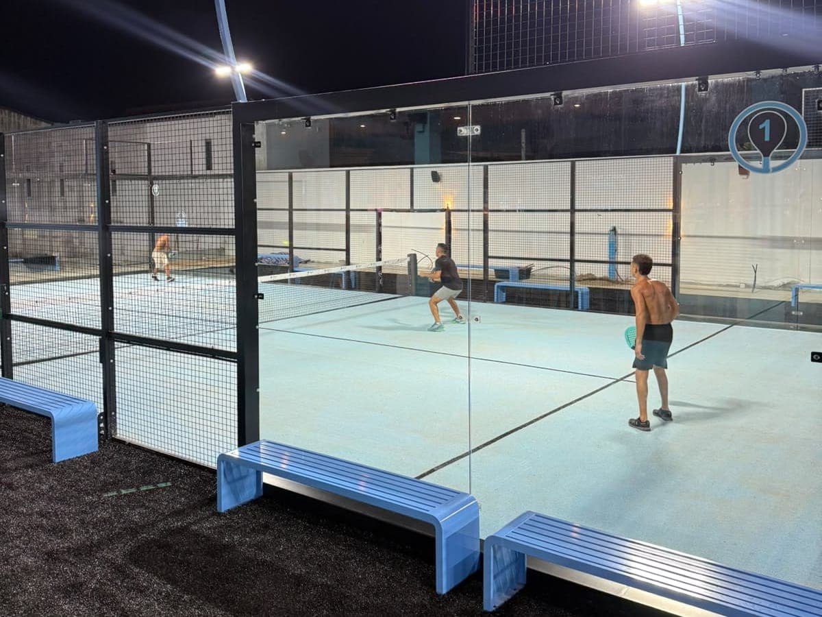 Players on the floodlit open-air court 1, behind glass walls, at night